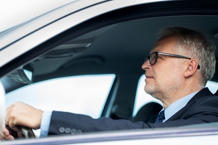 transport, business trip and people concept - happy senior businessman driving car