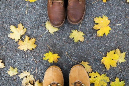 season and people concept - couple of feet in boots with autumn leaves on groundの写真素材