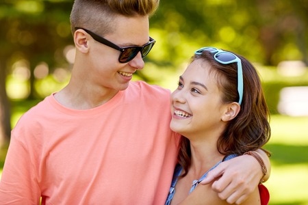 holidays, vacation, love and people concept - happy smiling teenage couple hugging and looking at each other at summer parkの写真素材