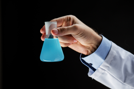 science, chemistry, research and people concept - close up of scientist hand holding test flask with chemical over black backgroundの写真素材