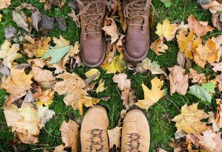 season and people concept - couple of feet in boots with autumn leaves on ground