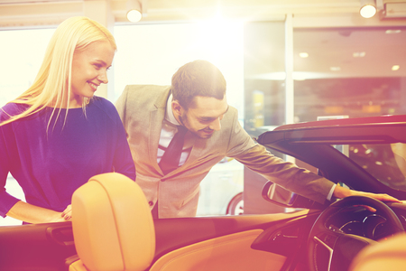 auto business, car sale, consumerism and people concept - happy couple buying car in auto show or salonの写真素材