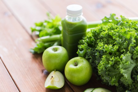 healthy eating, food, dieting and vegetarian concept - bottle with green juice, fruits and vegetables on wooden tableの写真素材
