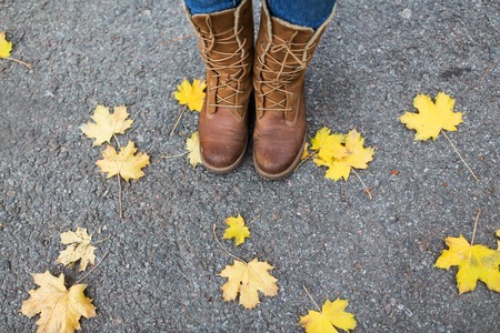 season, footwear and people concept - female feet in boots with autumn leaves on ground
