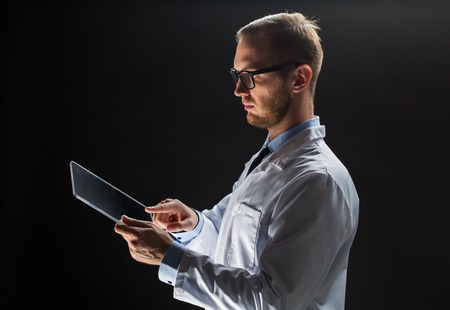 people, science, technology and medicine concept - close up of male doctor or scientist in white coat with tablet pc computer over black backgroundの写真素材