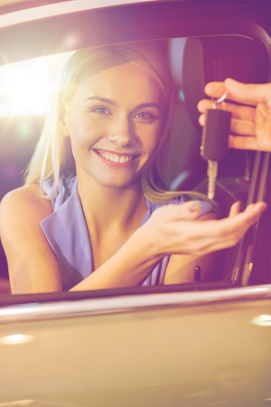 auto business, car sale, consumerism and people concept - happy woman taking car key from dealer in...