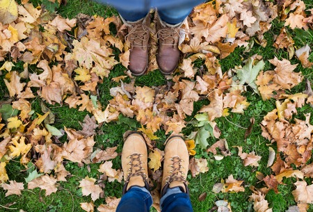 season and people concept - couple of feet in boots with autumn leaves on groundの写真素材
