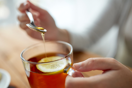 healthy food, eating and ethnoscience concept - close up of woman adding honey to tea cup with lemonの写真素材