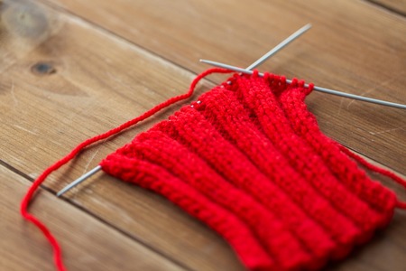handicraft and needlework concept - hand-knitted item with knitting needles on woodの写真素材