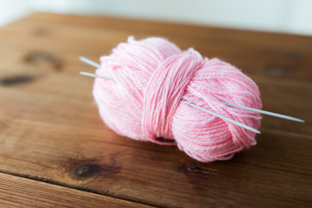 handicraft and needlework concept - knitting needles and ball of pink yarn on wood