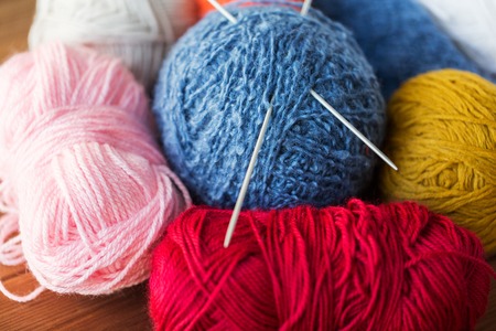 handicraft and needlework concept - knitting needles and balls of yarn on woodの写真素材