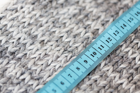 handicraft, knitwear and needlework concept - close up of knitted item with measuring tape