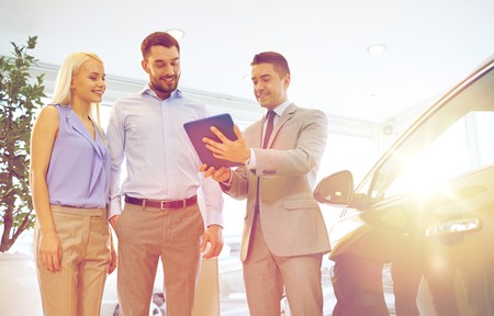 auto business, car sale, technology and people concept - happy couple with car dealer in auto show...
