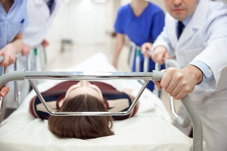 profession, people, healthcare, reanimation and medicine concept - group of medics or doctors carrying unconscious woman patient on hospital gurney to emergency roomの写真素材