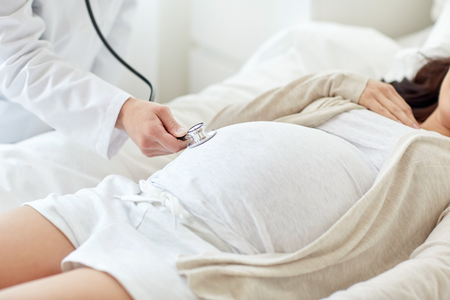 pregnancy, medicine, healthcare and people concept - close up of obstetrician doctor with stethoscope listening to pregnant woman baby heartbeat at hospitalの写真素材