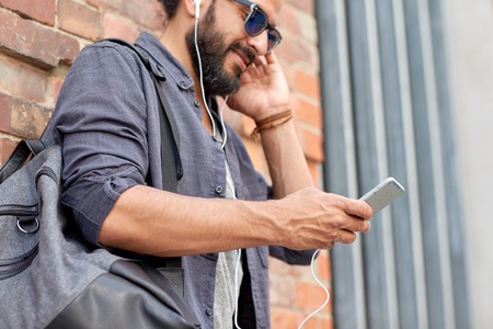 people, technology, travel and tourism concept - close up of man with earphones, smartphone and bag listening to music on streetの写真素材