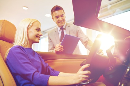 auto business, car sale, technology and people concept - happy woman and car dealer with tablet pc computer in auto show or salonの写真素材