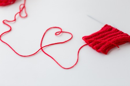handicraft, love, valentines day and needlework concept - hand-knitted item with knitting needles...