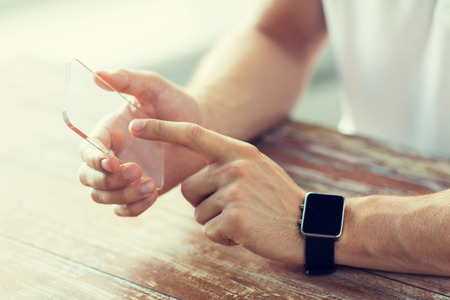 business, technology and people concept - close up of male hand holding and showing transparent smart phone and watch at homeの写真素材