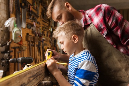 family, carpentry, woodwork and people concept - father and little son with ruler and pencil measuring wood plank at workshopの写真素材