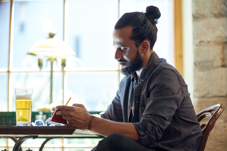 people, inspiration, freelance and leisure concept - close up of man with beer writing to notebook at bar or pubの写真素材