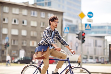 people, style, leisure and lifestyle - young hipster man with shoulder bag and earphones riding fixed gear bike on city streetの写真素材