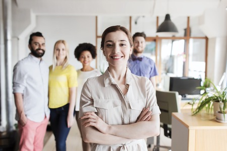 business, startup, people and teamwork concept - happy young woman over creative team in officeの写真素材