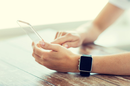 business, technology and people concept - close up of woman hand holding and showing transparent smart phone and watch at officeの写真素材
