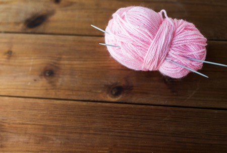 handicraft and needlework concept - knitting needles and ball of pink yarn on woodの写真素材