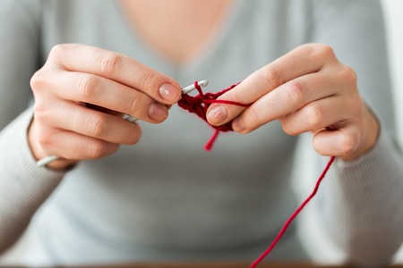 people and needlework concept - woman hands knitting with crochet hook and red yarnの写真素材