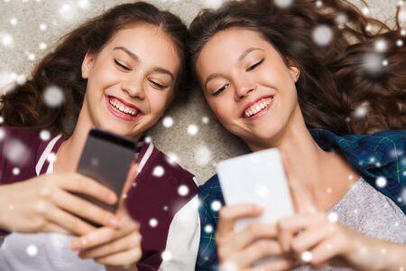 people, winter, christmas, technology and friendship concept - happy smiling pretty teenage girls or...