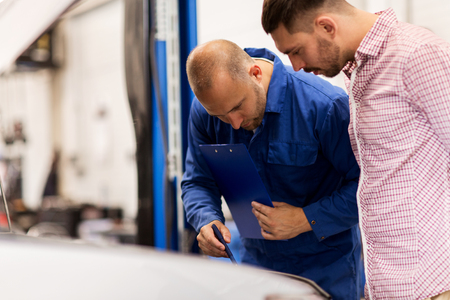 auto service, repair, maintenance and people concept - mechanic with clipboard and man or owner looking at broken car at shopの写真素材