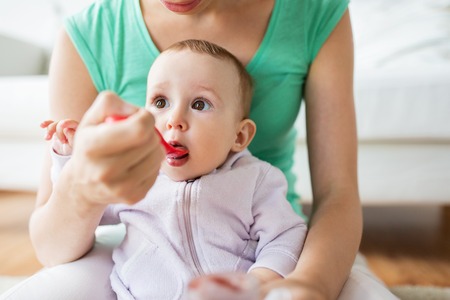 family, child, eating and parenthood concept - mother with spoon feeding little baby at homeの写真素材