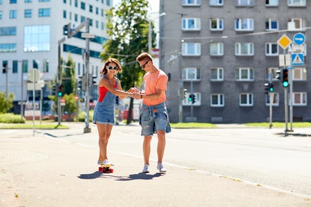 summer holidays, extreme sport and people concept - happy teenage couple riding short modern cruiser skateboard on city streetの写真素材