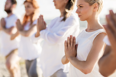 fitness, sport, and healthy lifestyle concept - group of people making yoga on beachの写真素材