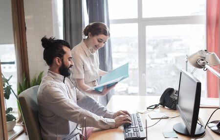 business, startup and people concept - happy creative team with computer and folder in office