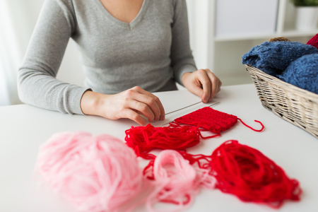 people and needlework concept - woman hands holding knitting needles and basket with yarn on table at homeの写真素材