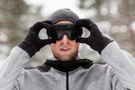 fitness, winter sport, people and healthy lifestyle concept - young man in ski goggles outdoorsの写真素材