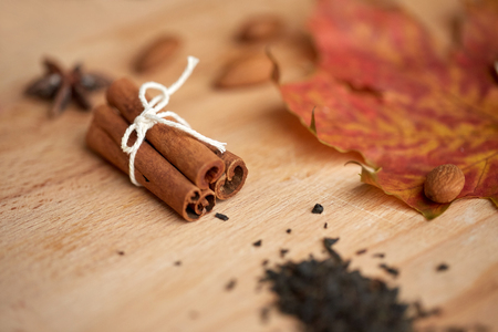 cooking, spice and ethnoscience concept - cinnamon, maple leaf and almond on wooden board