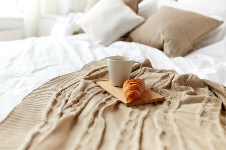 breakfast, coziness, morning, holidays and winter concept - cozy bedroom with coffee cup and croissant on wooden board in bed at homeの写真素材