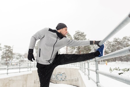 fitness, sport, people, exercising and healthy lifestyle concept - young man stretching leg and...