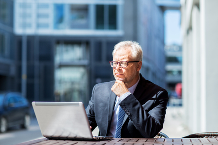 business, technology and people concept - senior businessman with laptop computer at city street cafeの写真素材