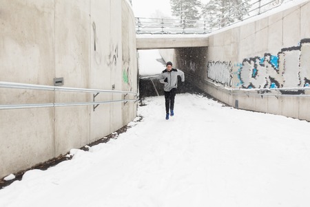 fitness, sport, people, season and healthy lifestyle concept - young man running out of pedestrian subway tunnel in winterの写真素材