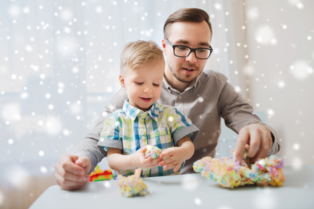 family, childhood, creativity, activity and people concept - happy father and little son playing with ball clay at home over snowの写真素材