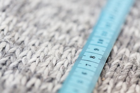 handicraft, knitwear and needlework concept - close up of knitted item with measuring tapeの写真素材
