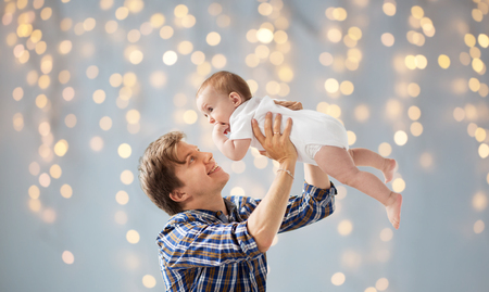 family, fatherhood and parenthood concept - happy smiling young father with little baby over holidays lights backgroundの写真素材