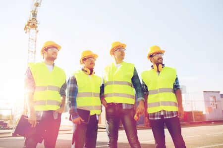 business, building, teamwork, technology and people concept - group of smiling builders in hardhats with tablet pc computer and clipboard outdoorsの写真素材