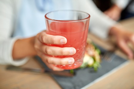 food, drink, eating and people concept - hand of woman with glass of juice and salad at restaurantの写真素材