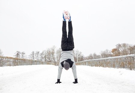 fitness, sport, training, people and exercising concept - young man on doing handstand outdoors in...