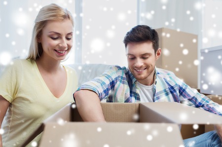 moving, people, repair and real estate concept - smiling couple looking into big cardboard box at new home over snowの写真素材